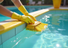 Main gantée nettoyant les murs jaunes de la piscine